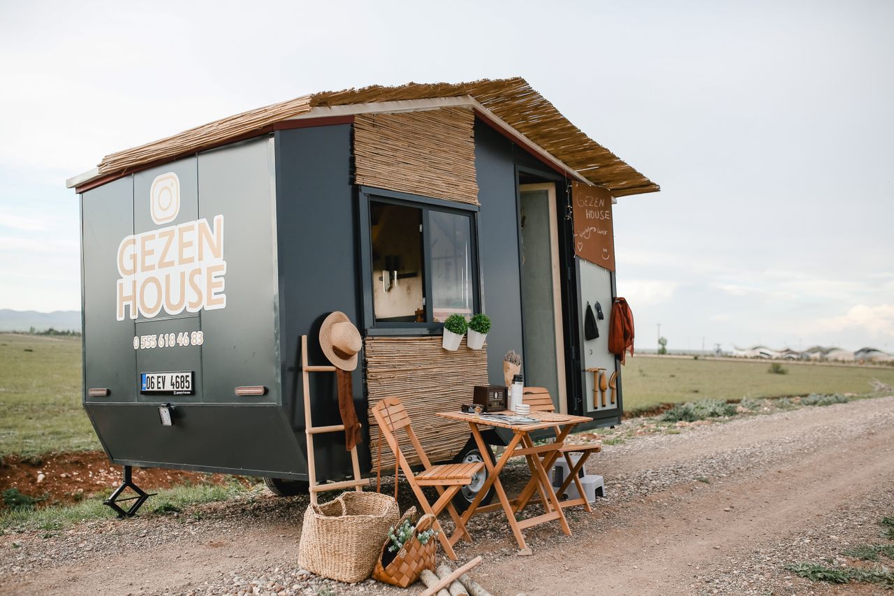 Mobile tiny house with outdoor furniture on a countryside dirt road.
